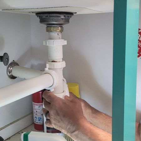 Professional Plumber working on kitchen utilities under sink stopping a water leak in repairs.